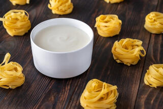 bechamel sauce served in a bowl with tagliatelle beside