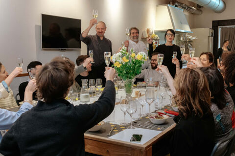 group of people cheers with prosecco at dining table with chefs