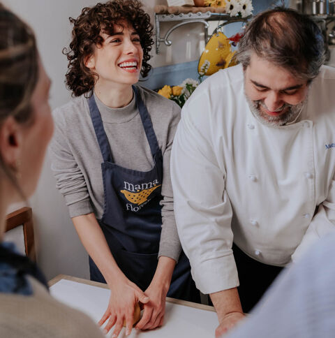 young woman laughs making pizza dough alongside chef