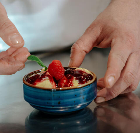 chefs hands decorating ice cream with raspberries and mint