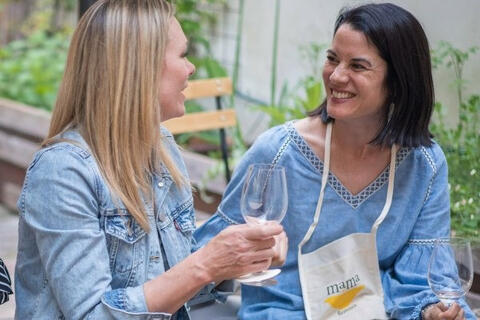 two women smiling with glasses of wine in hand outdoors