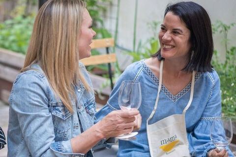 two women sat outside with wine glasses smiling