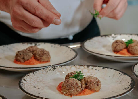 chefs hands plate meatballs with tomato sauce and herbs