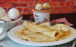 crepes on a plate with eggs in the background and icing sugar