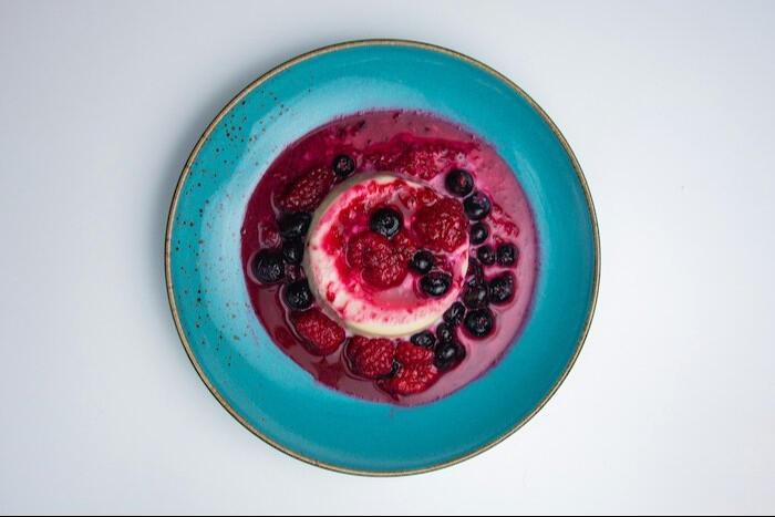 pana cotta with red berries on a blue plate