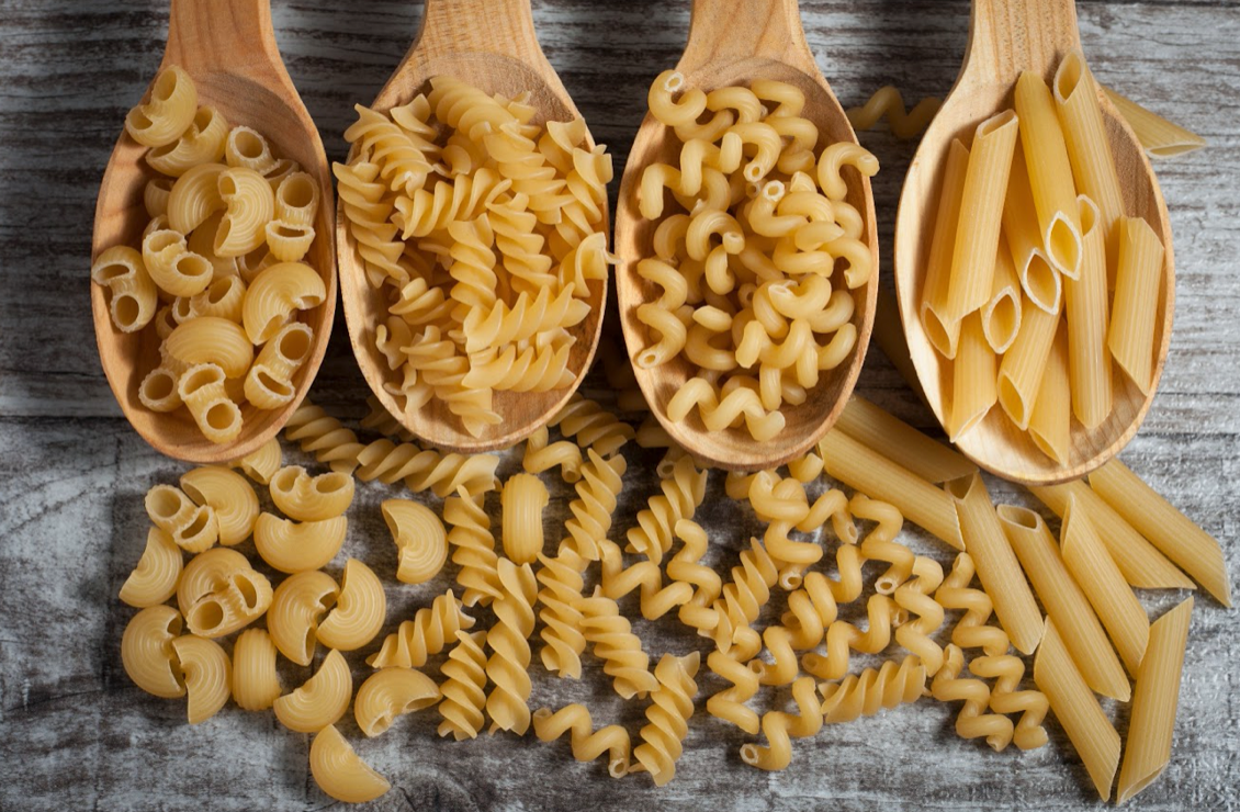 mixed selection of dried pasta shapes displayed on wooden spoons