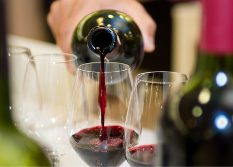 person pouring red wine into wine glass