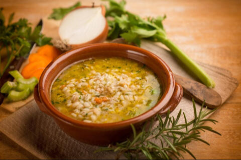 barely soup in a bowl served aside raw onion carrot and celery on a chopping board.
