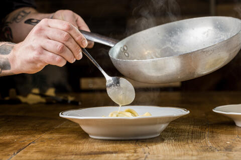 adding sauce to pasta dish with spoon