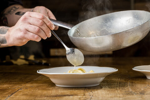 adding sauce to pasta dish with spoon
